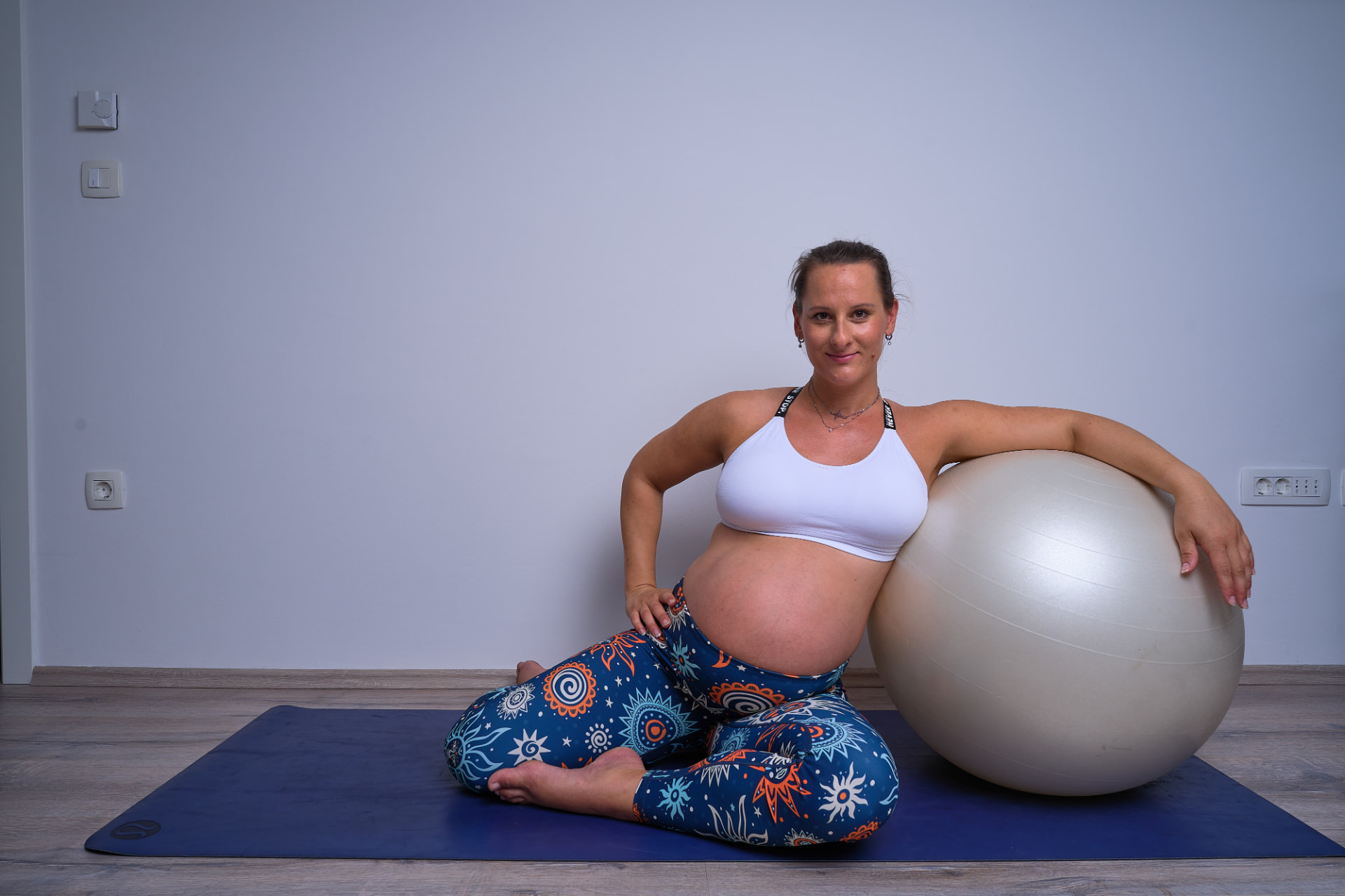 Trudnica u bijelom topu odmara uz pilates loptu na prostirci.